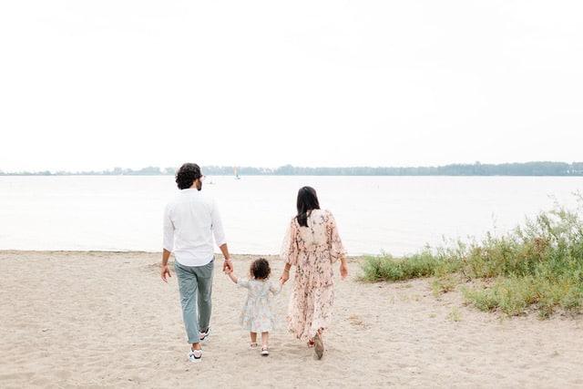 A young girl between her parents walking on the beach
