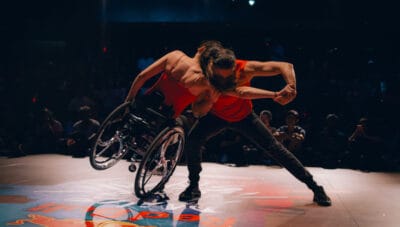 Two dancers, one in a wheelchair, performing on stage.