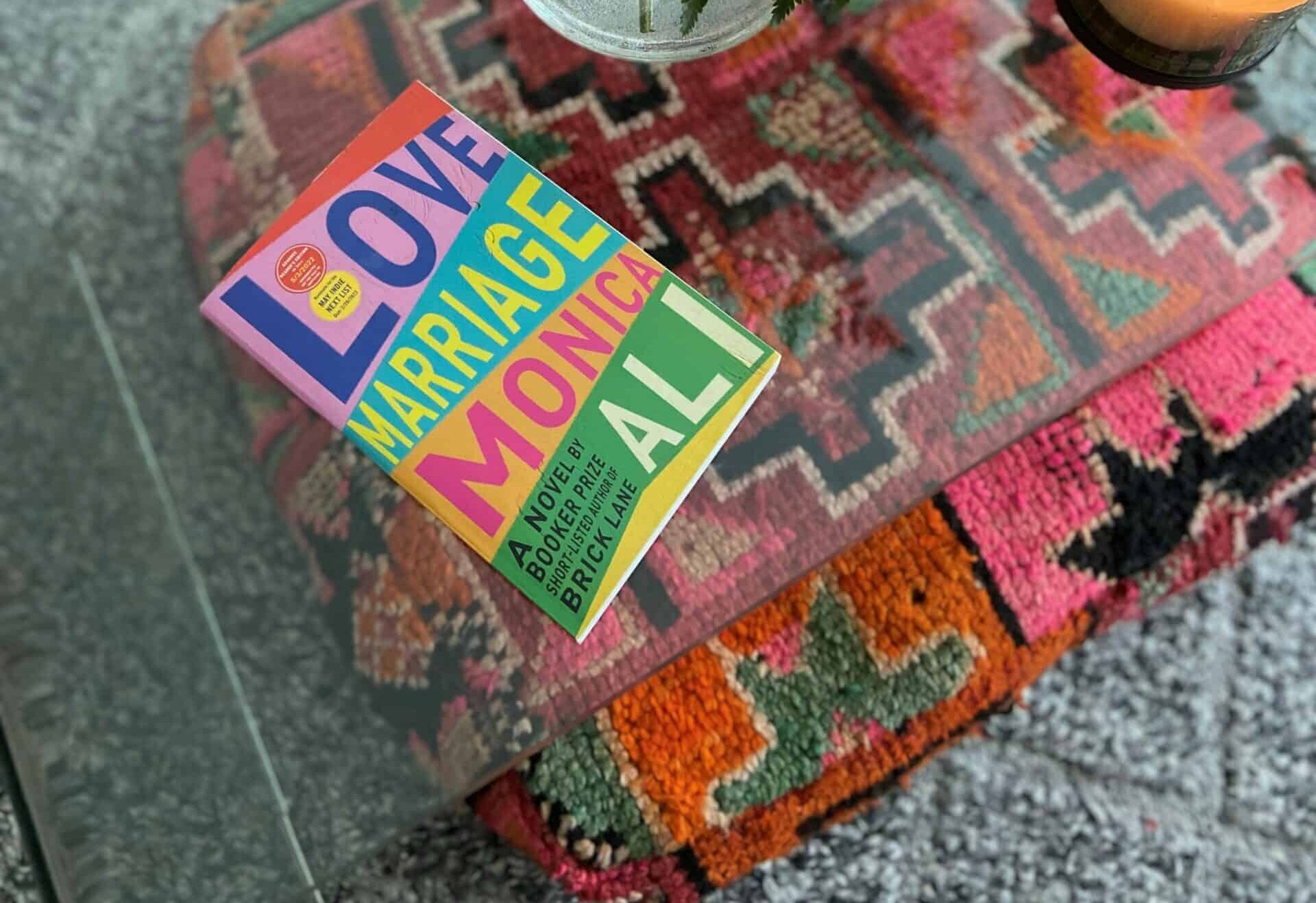 Love Marriage by Monica Ali placed on a table next to a candle and flower arrangement