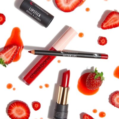 Red lipstick, lip gloss and lip liner on white background surrounded by strawberries