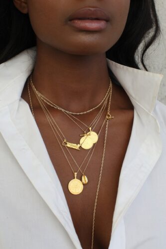 Closeup of a model's neck with several gold Omi Woods necklaces, including the Coffee Bean